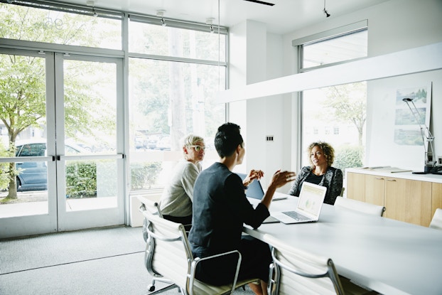  Team of three coworkers sitting at a table in a bright conference room.