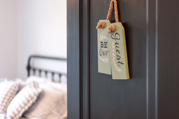  Bed and breakfast guest room with a sign on the door that says, "Be our guest."