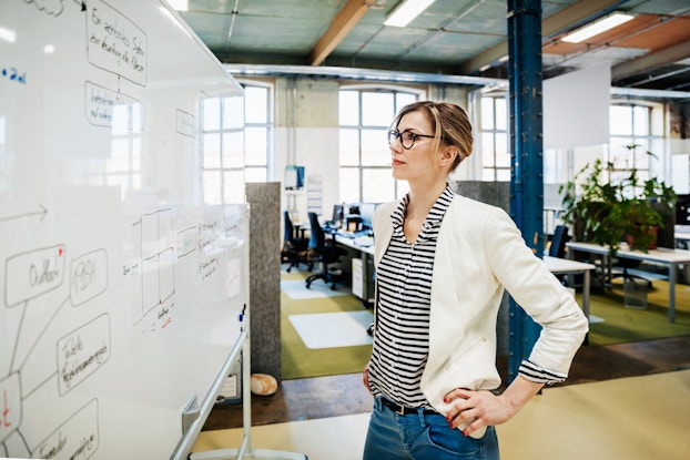 A businesswoman looks at a white board that contains plans and figures.
