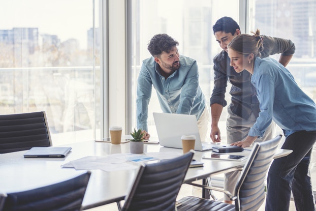 Three coworkers in a conference room hovered around a computer screen.