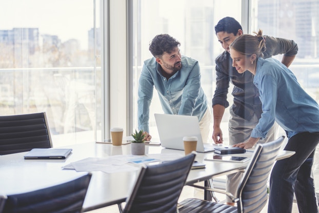  Three coworkers in a conference room hovered around a computer screen.