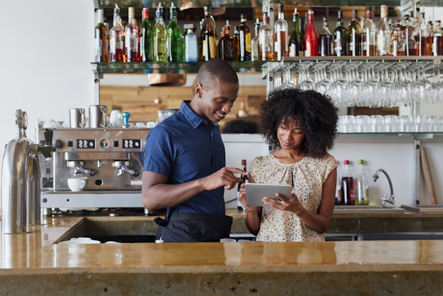 two businesspeople behind bar looking at tablet