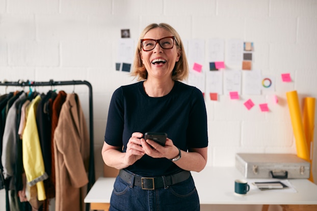 Business owner inside shop smiling and laughing while holding phone.