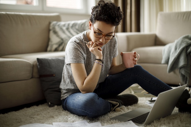  woman sitting on floor in home with laptop and coffee