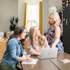 a group of women sitting at a table looking at a laptop