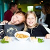 two girls sitting at a table with food and drinks