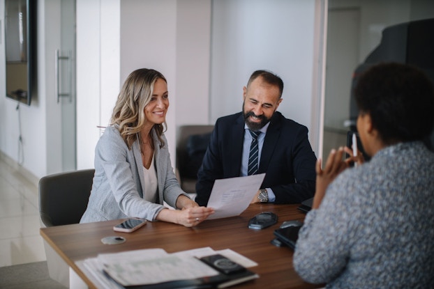 A middle-age couple is is seated at a desk with their bank loan officer. They are reviewing loan terms for a small business loan they are seeking.