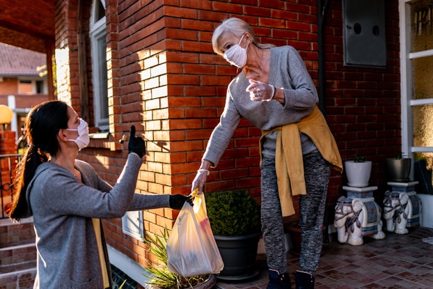  woman delivering groceries to another woman with masks on