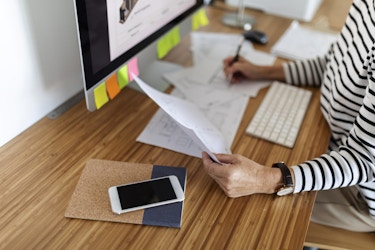 Image of a woman's hands at her desk holding papers and a pen.