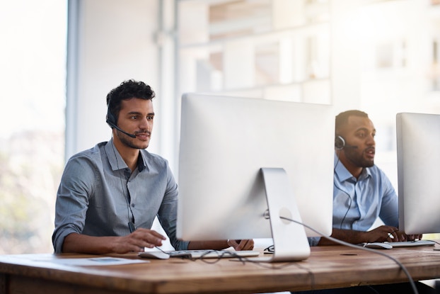 two male coworkers with headsets on laptops