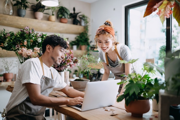 Two coworkers in their plant shop looking at a laptop screen.