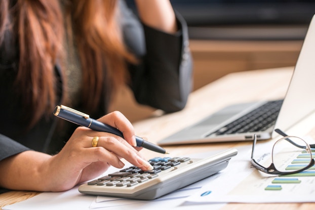 Close-up photo of a woman holding a pen and entering numbers on a calculator. She is calculating the return on investment for a business item.