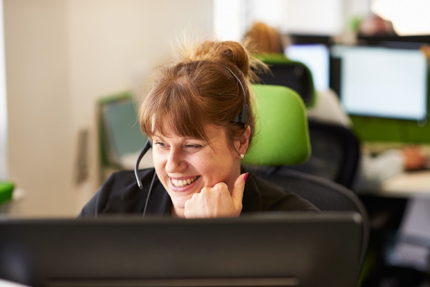  A woman working in a call center smiles while talking on the phone with a customer.