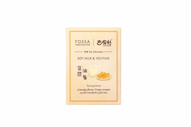 A box of Fossa chocolate. The box is cream-colored and bears a picture of the chocolate's flavoring -- in this case, a glass of soy milk and a plate of youtiao fried dough. The text below the picture reads "Tasting Notes" and "A nostalgic flavour. Creamy, aromatic soy with crunchy bits of you tiao."