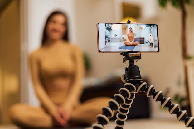  Woman sitting on a yoga mat wearing workout clothing and recording herself.
