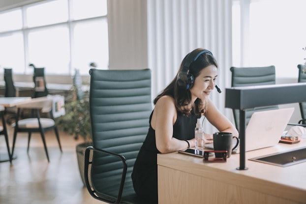A woman is pictured in an office talking on a phone headset with a client.