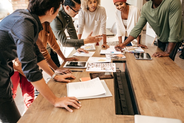 Team of employees standing around a long table going over strategy documents.