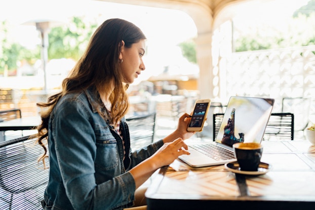 Woman sitting in a cafe on laptop and phone.