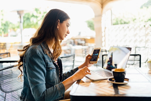  Woman sitting in a cafe on laptop and phone.