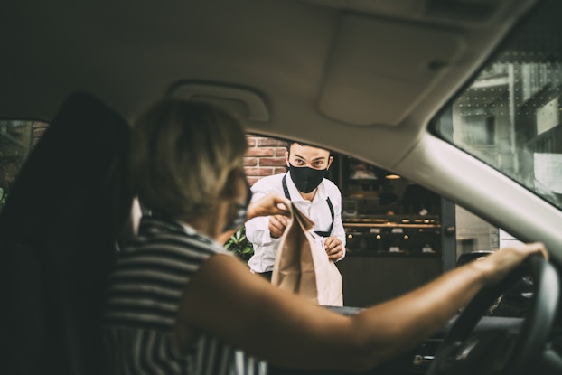  woman picking up curbside takeout from man at restaurant