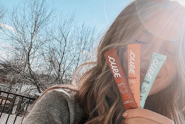 Influencer holding three Cure Hydration packets in front of her face.