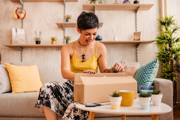  Woman happily unboxing a package inside her home.