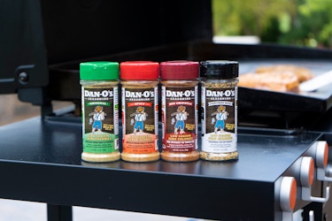  Four seasoning blends by Dan-O's Seasoning in a row on the side table of a barbecue. 