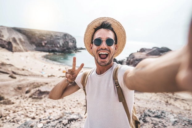  Happy person on a beach vacation wearing a hat and sunglasses and taking a selfie.