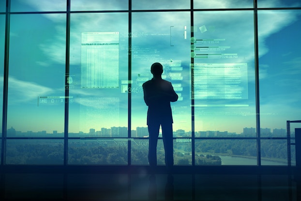 man looking out window with coding text in background
