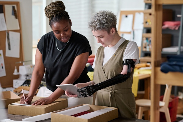 Two young warehouse workers check a customer's shipping address while one of them writing it down on top of package.