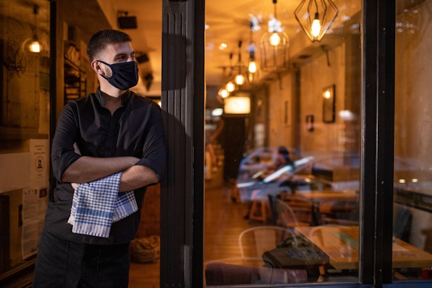  Business owner standing outside restaurant wearing a mask.