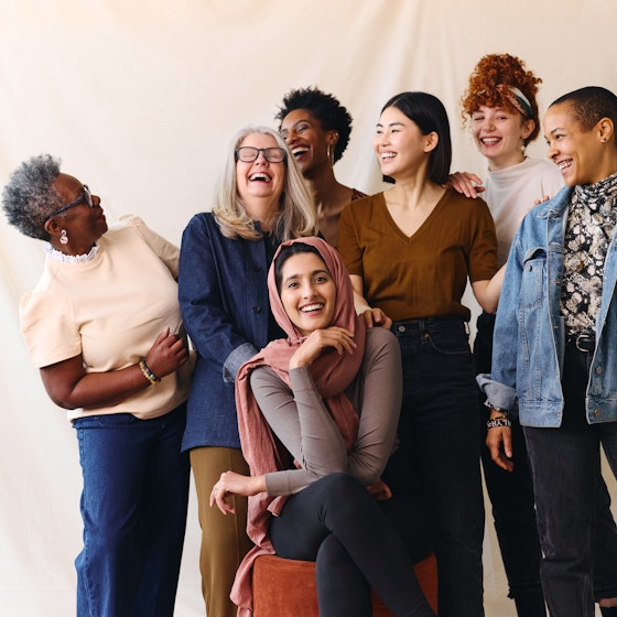  Group of diverse people standing in front of a beige backdrop smiling and laughing. 