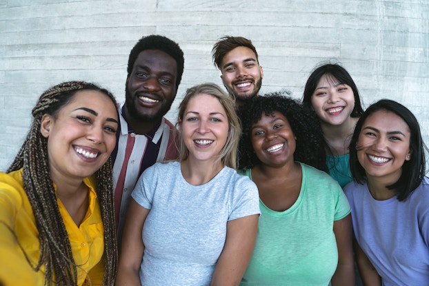  A diverse group of people stands shoulder-to-shoulder, smiling.