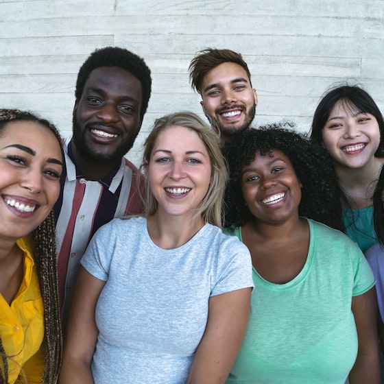 A diverse group of people stands shoulder-to-shoulder, smiling.