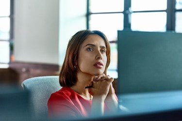  A business executive is seated in front a computer. She looks at information on her computer and contemplates a question. 