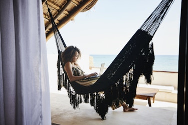  Woman relaxing on a hammock while working on a laptop. 