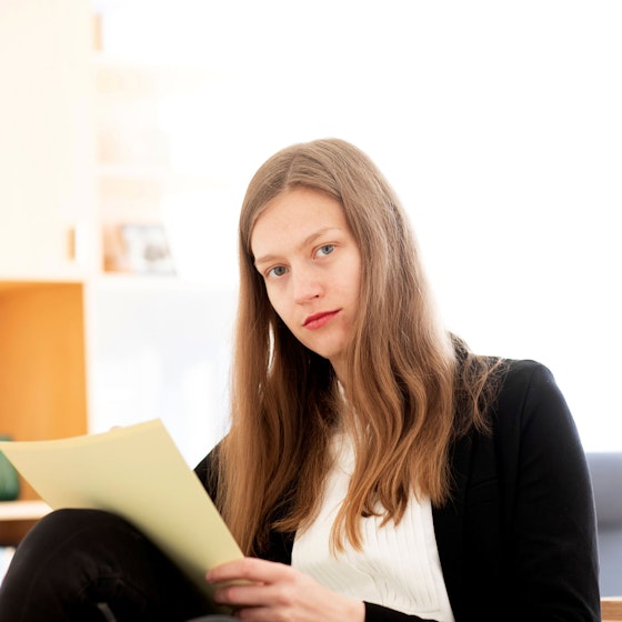 A young business woman looks at the viewer. She is holding papers in her hand and reviewing documents.