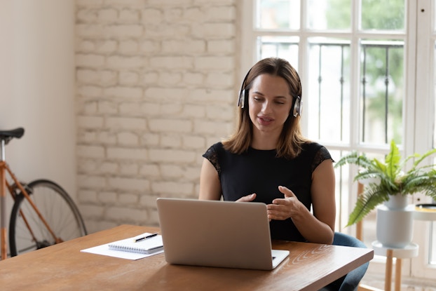 woman working on laptop and using headset at kitchen table