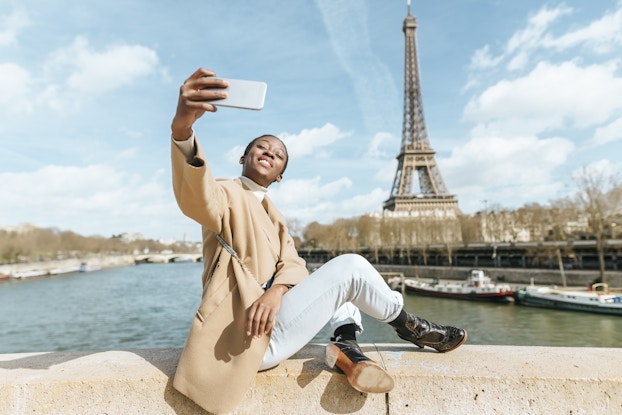 Woman in Paris taking a selfie with the Eiffel Tower behind her.