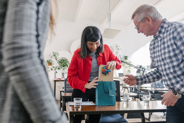 A woman receives a gift in a bag from her manager.