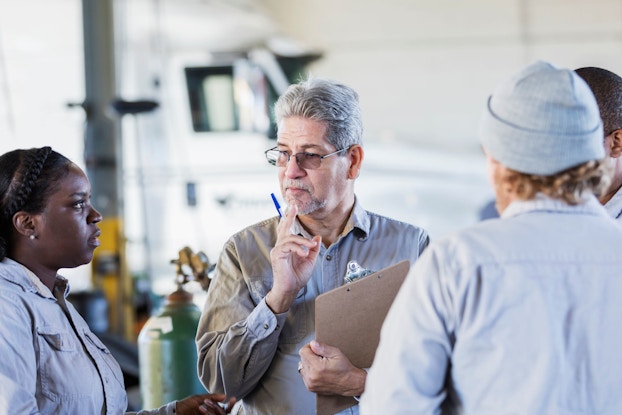 Four workers in a repair shop stand together and have an informal meeting.