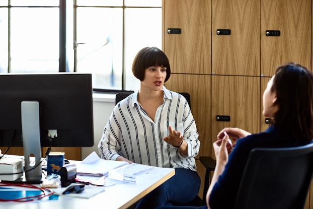 A woman seated in an office having a one-on-one meeting with a female employee.