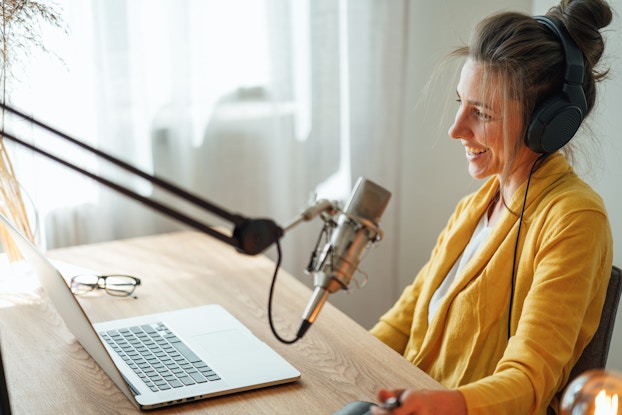  Woman smiling in home office recording a podcast.