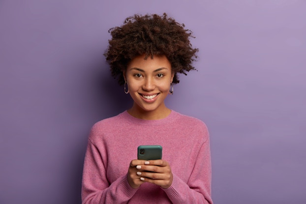  Woman standing on phone in front of a purple background.