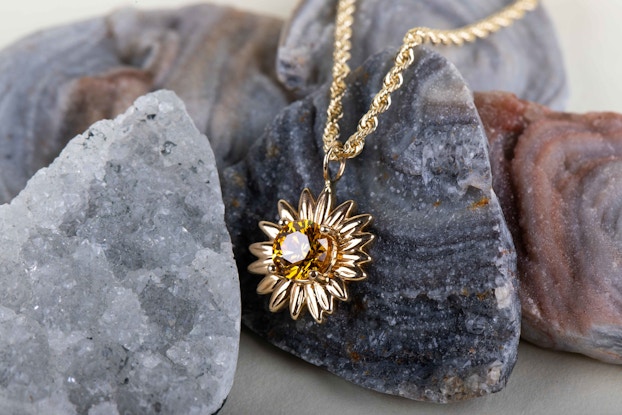  A yellow gold and diamond necklace created by Eterneva displayed on stones.