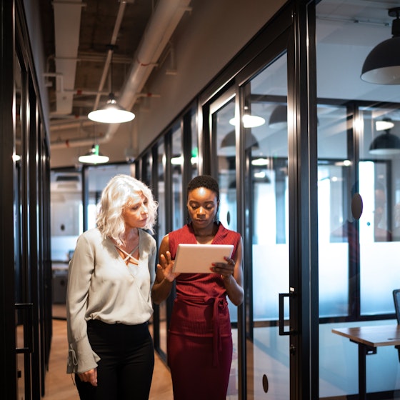 Two coworkers looking at tablet as they walk through an office hall.