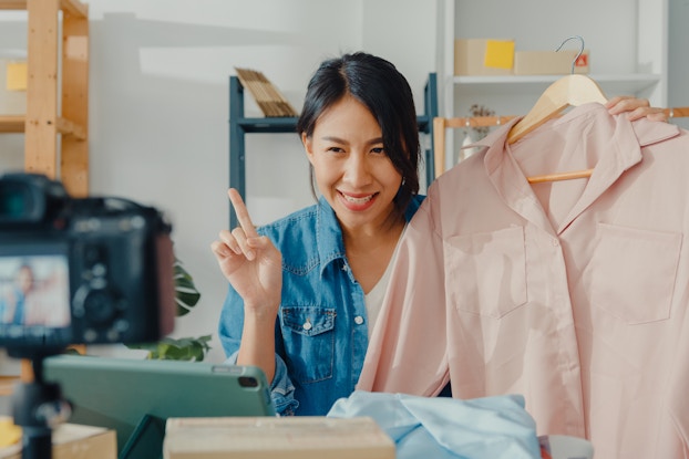 Woman recording a video in her workplace holding clothing.