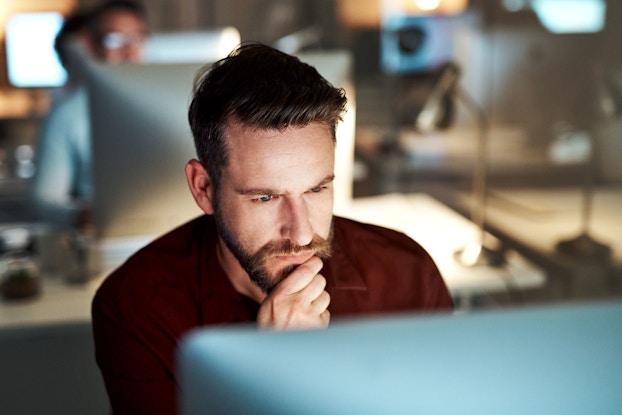  A close-up image shows a businessman with a beard as he looks at this desktop computer monitor and contemplates something.
