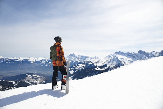  Person standing and looking out on a snowy mountain, holding a snowboard.