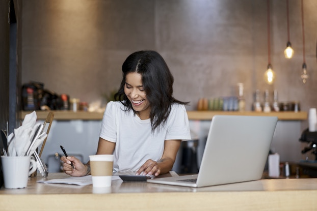 Smiling woman working at a laptop inside her shop.
